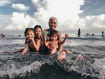 A photo of a Filipino grandparent with her grandchildren in the water at a beach